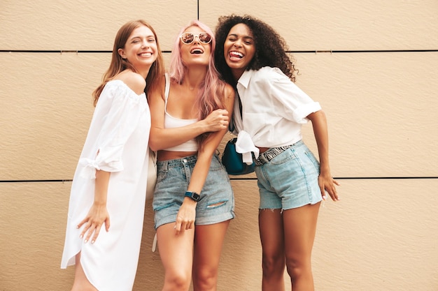 Three young beautiful smiling hipster female in trendy summer clothesSexy carefree multiracial women posing on the street backgroundPositive models having fun in sunglasses Cheerful and happy