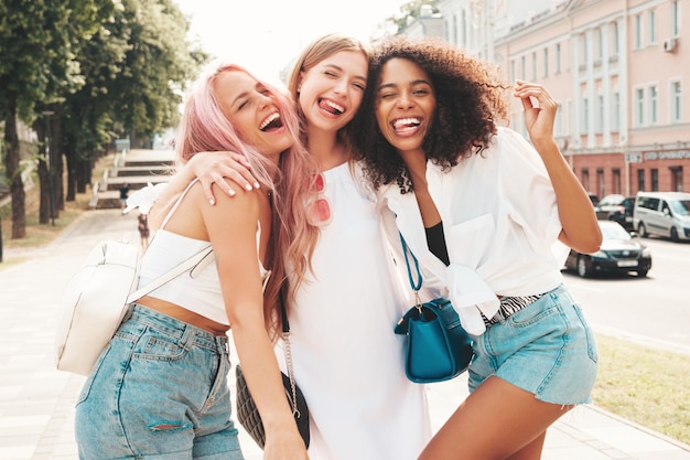 Three young beautiful smiling hipster female in trendy summer clothesSexy carefree multiracial women posing on the street backgroundPositive models having fun in sunglasses Cheerful and happy