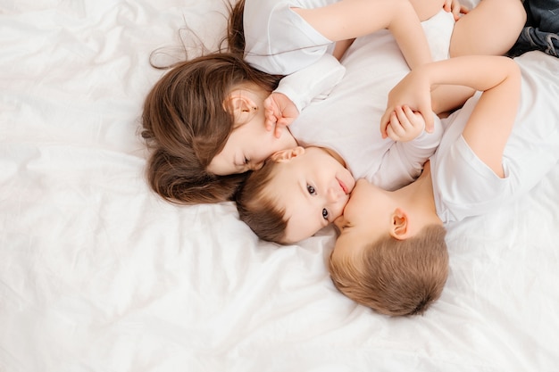 Three young children lie in bed and cuddle