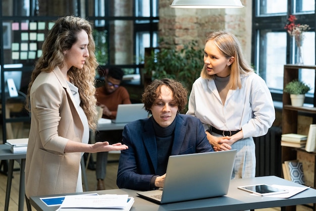 Three young confident colleagues discussing data on laptop screen