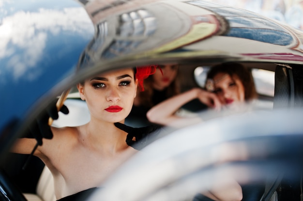 Three young girl in retro style dress seat on old classic vintage car. Amazing view of sexy women.