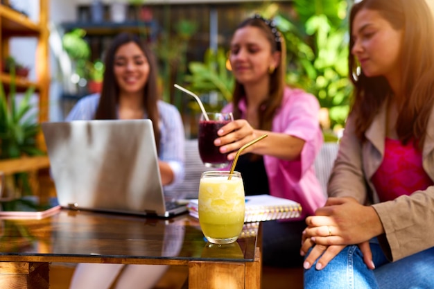 Three young latin women working with a laptop in a cafe out of focus drinking juice