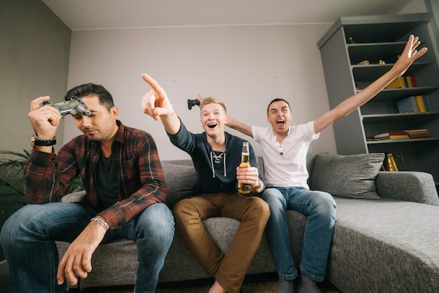 Three young men with joysticks play in football game on tv