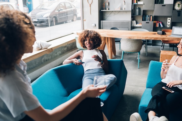 Three young multiracial women sitting in modern pub and drinking together