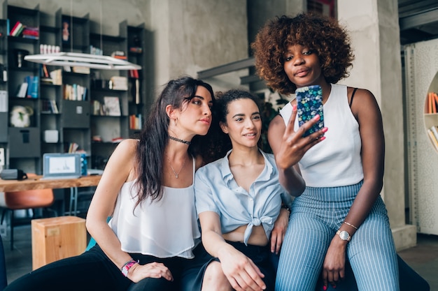 Three young multiracial women using smartphone and posing together