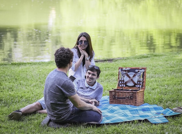 Three young people at a picnic in a park near a lake