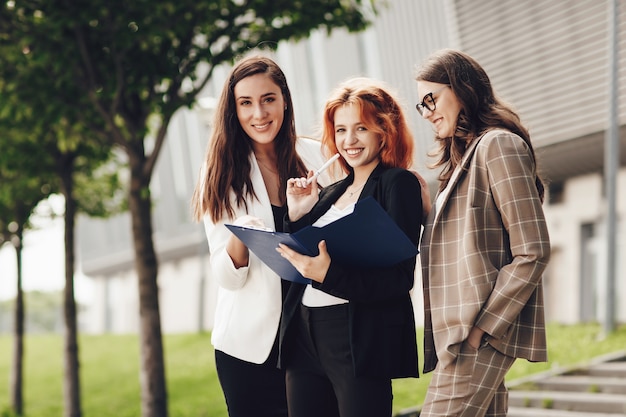 Three young stylish women working outdoors and smiling, hold a folder with documents