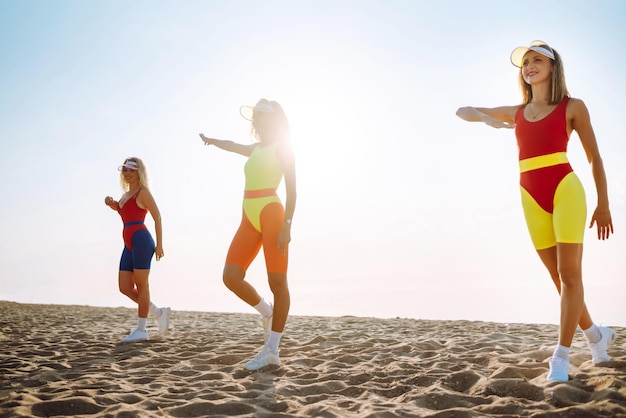 Photo three young woman dancer dancing in bright swimsuits on the beach sport fitness active life