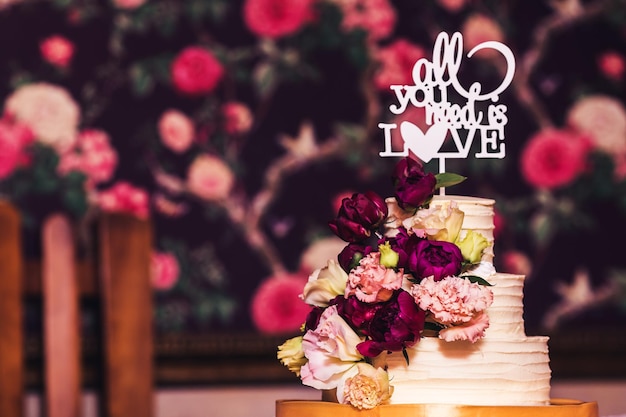 Threetiered wedding cake decorated with beautiful flowers and wooden inscription all you need is love