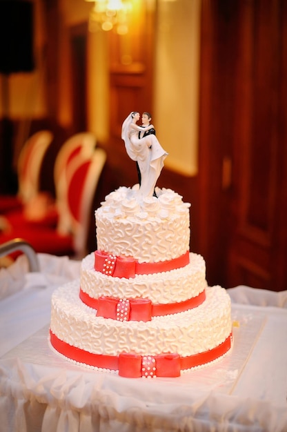 Threetiered white wedding cake with red ribbons