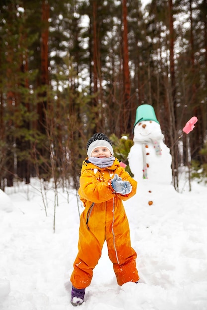 Threeyearold girl in orange jumpsuit with snowman outside in winter