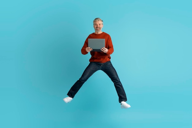 Thrilled middle aged man jumping in the air with laptop