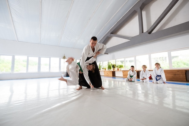 Throwing girl. Aikido trainer throwing girl in white kimono while teaching her to protect herself