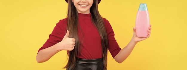 Thumb up happy girl in hat hold shampoo presenting cosmetic product for teen