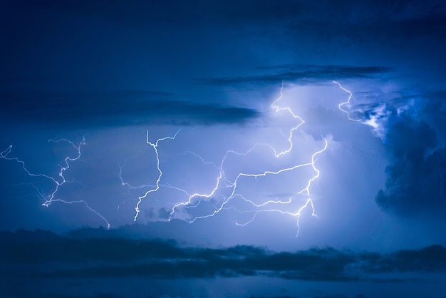 Thunder storm lightning strike on the dark cloudy sky background at night.