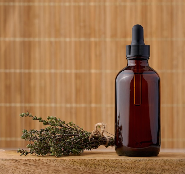 Thyme essential oil in glass bottle with dropper and fresh thyme sprigs on table cosmetic ingredient