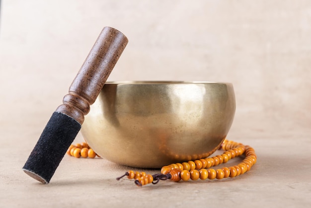 Tibetan singing bowl with stick mala beads strands used during mantra meditations on beige stone background