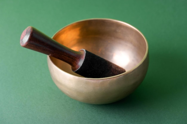 Tibetan singing bowl with sticks used during mantra meditations on green background close up