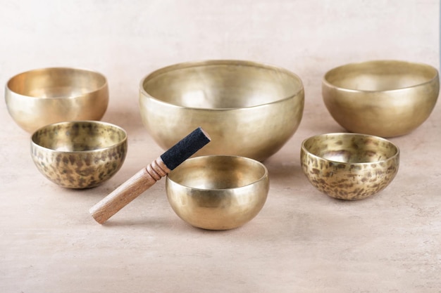 Tibetan singing bowls with sticks used during mantra meditations on beige stone background close up