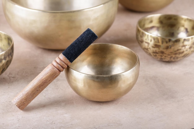 Tibetan singing bowls with sticks used during mantra meditations on beige stone background close up