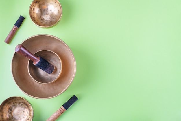 Tibetan singing bowls with sticks used during mantra meditations on green background flat lay web banner