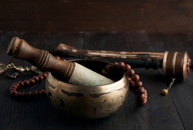 Tibetan singing copper bowl with a wooden clapper on a brown wooden table, objects for meditation and alternative medicine