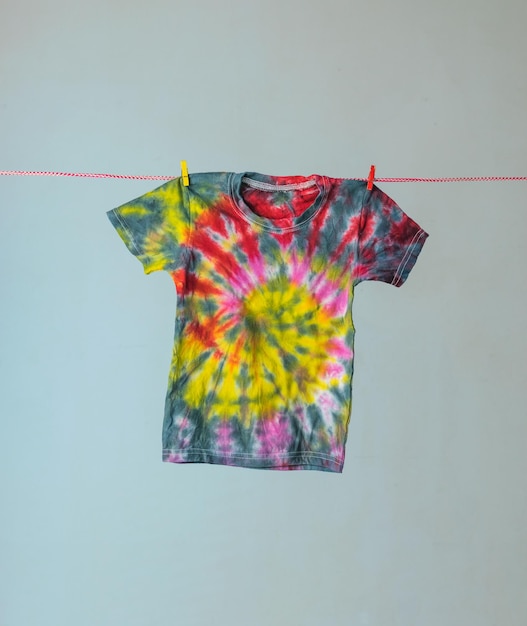 A tie dye-colored T-shirt is drying on a clothesline. Making clothes at home. Flat lay.