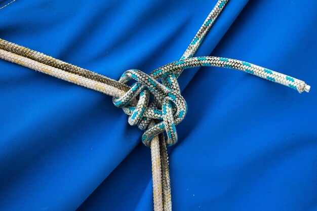 Photo tied ropes in a knot in the middle on a blue sailcloth closeup nautical knot made of ropes on canvas