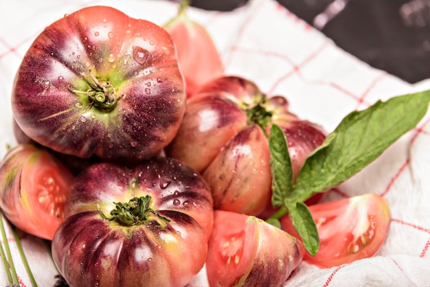 Tiger tomato on a cutting board with basil leaves on wooden background Fresh tomato wased for cooking Tomato with droplets of water