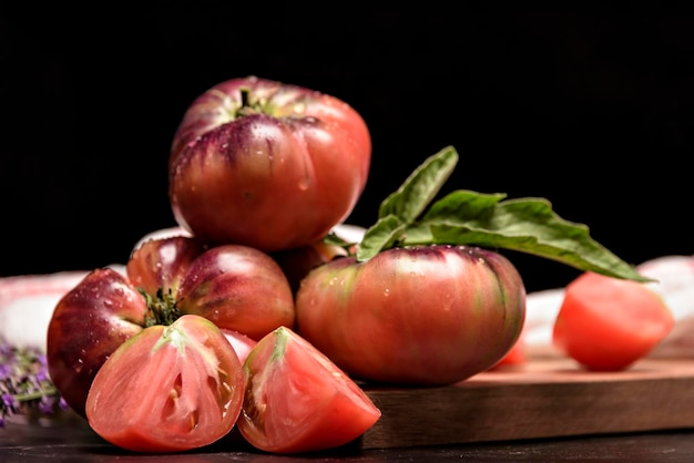 Tiger tomato on a cutting board with basil leaves on wooden background Fresh tomato wased for cooking Tomato with droplets of water