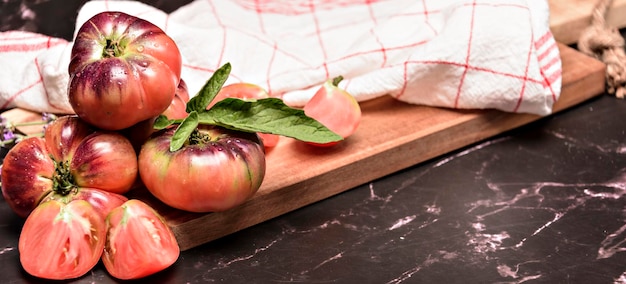 Tiger tomato on a cutting board with basil leaves on wooden background Fresh tomato wased for cooking Tomato with droplets of water