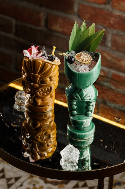 Tiki Drink Cocktails Two cocktails in different glasses against the background of a bar decorated with dried fruits and tropical leaves