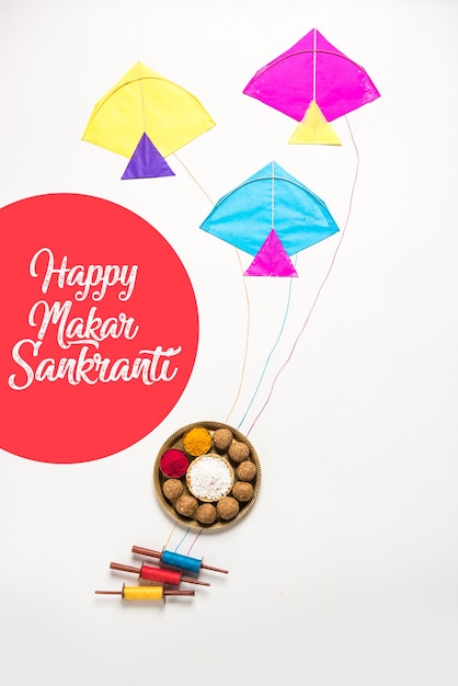 Til Gul OR Sweet Sesame Laddu with Miniature Fikri and Kite model with haldi Kumkum and sugar crystals for Makar Sankranti festival over moody background, selective focus