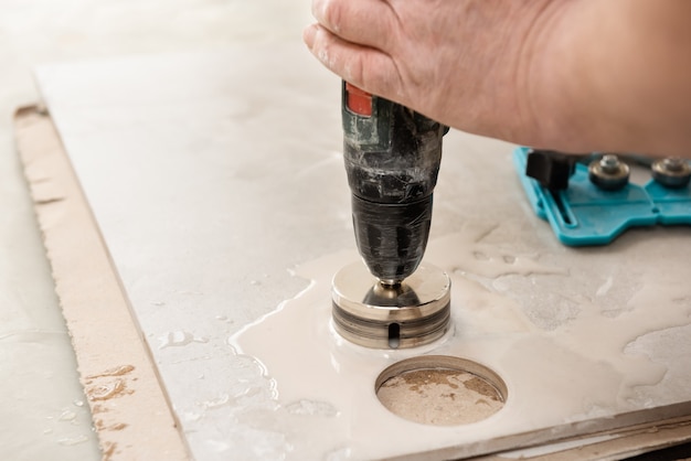 A tiler is using a diamond crown to drill holes in the ceramic tile close up