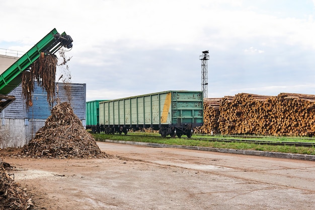 Timber yard with stacks of logs, open freight wagons and bark chipper