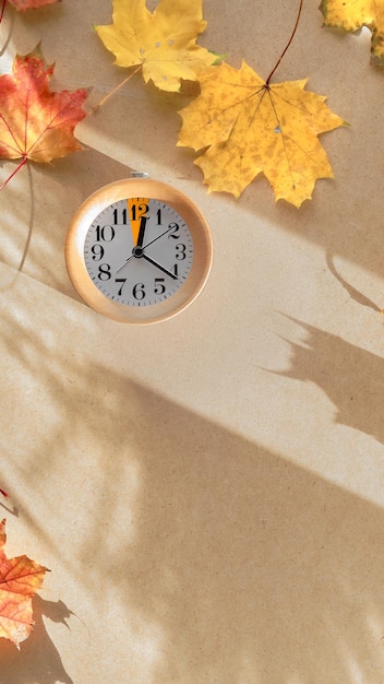 Time change in Autumn Text Fall Back on blackboard chalk board Wooden alarm clock with one hour mark with dry Fall leaves on recycled cardboard