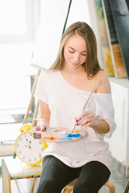 Time for creating. Attractive woman posing fullface while painting a sea-scape