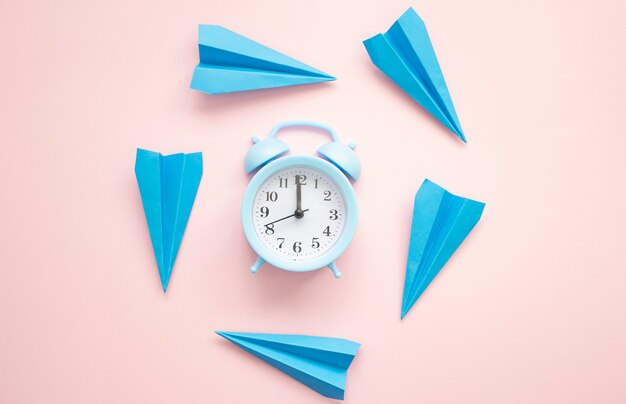 Time flying concept with blue paper airplanes and alarm clock on a pink surface.