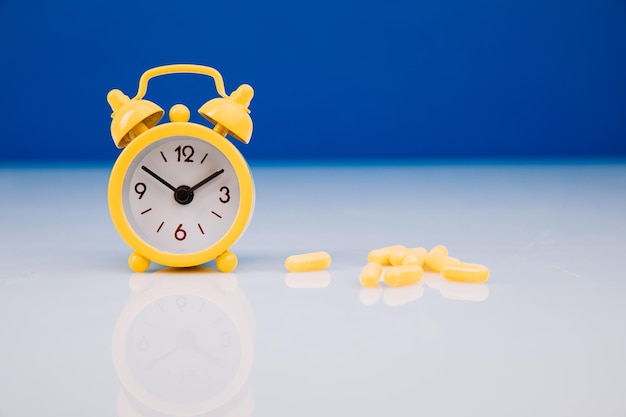 Time for health check concept Yellow alarm clock with pills closeup