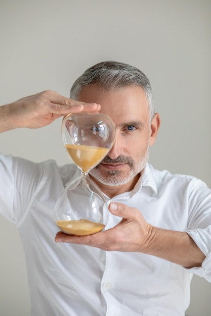 Time. A man in white shirt with a sand watch in hands