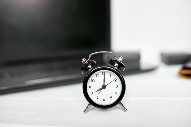 Time management concept, office workplace, notebook, computer, laptop and black alarm clock on white wooden office desk, copy space.