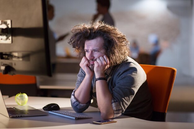 A time for relax. Young tired casual businessman relaxing at the desk in his night office