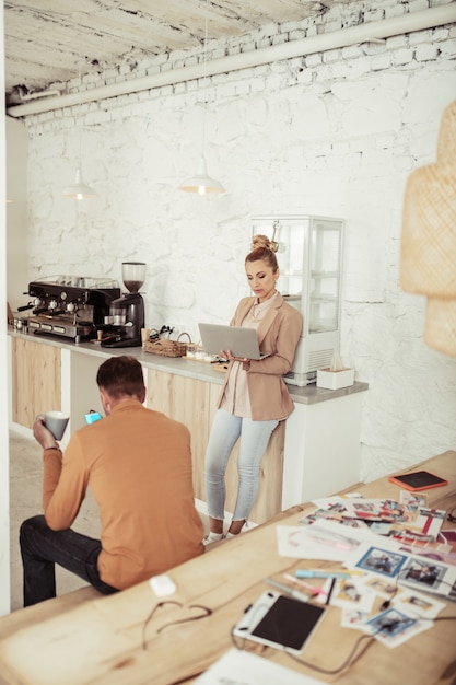 Time to rest. Fashion designer sitting on a bench with a cup of coffee and his assistant standing in front of him with a laptop during their coffee break.