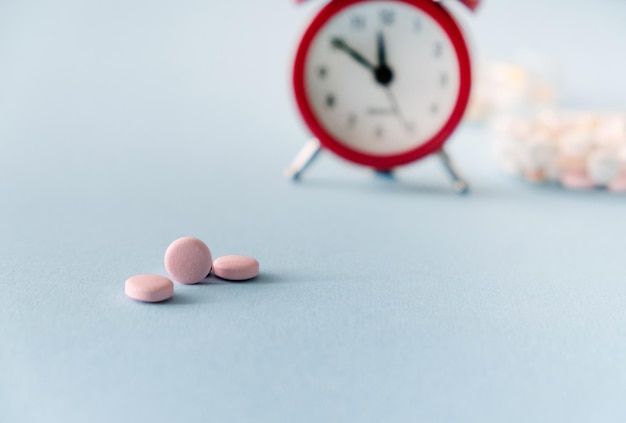 Time to take pills Alarm clock and pills on blue background Right time for using medicines