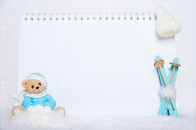 Time for winter holidays Blank notepad teddy bear with snowballs toy wooden blue skis and white hat on snowy background