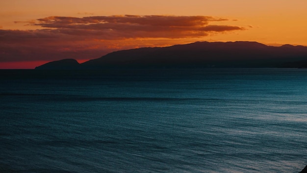 Timelapse of dramatic orange sunset over sea with mountains on summer evening