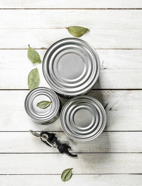 Tin cans with food and opener. On a white wooden table.