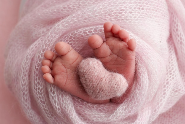 The tiny foot of a newborn baby Soft feet of a new born in a pink wool blanket Close up of toes heels and feet of a newborn Knitted pink heart in the legs of a baby Studio macro photography