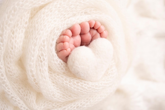 The tiny foot of a newborn baby Soft feet of a new born in a white wool blanket Close up of toes heels and feet of a newborn Knitted white heart in the legs of a baby Macro photography