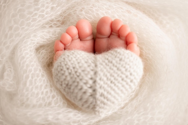 The tiny foot of a newborn baby Soft feet of a new born in a white wool blanket Close up of toes heels and feet of a newborn Knitted white heart in the legs of a baby Macro photography